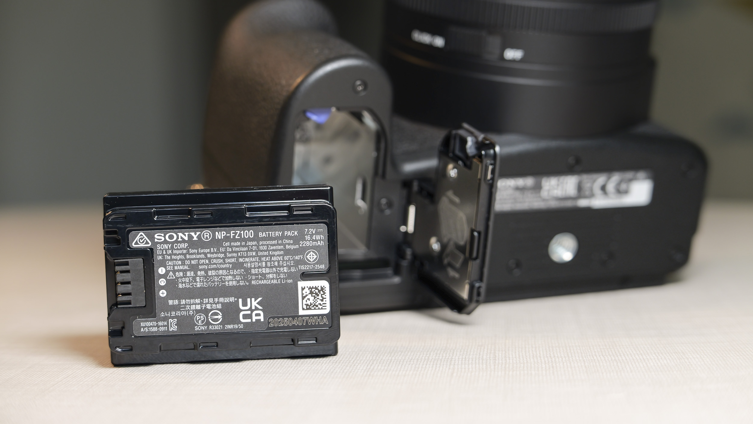 Closeup of the Sony RX10 V bridge camera's  battery door, and the battery has been removed and placed on the table in front  of the camera