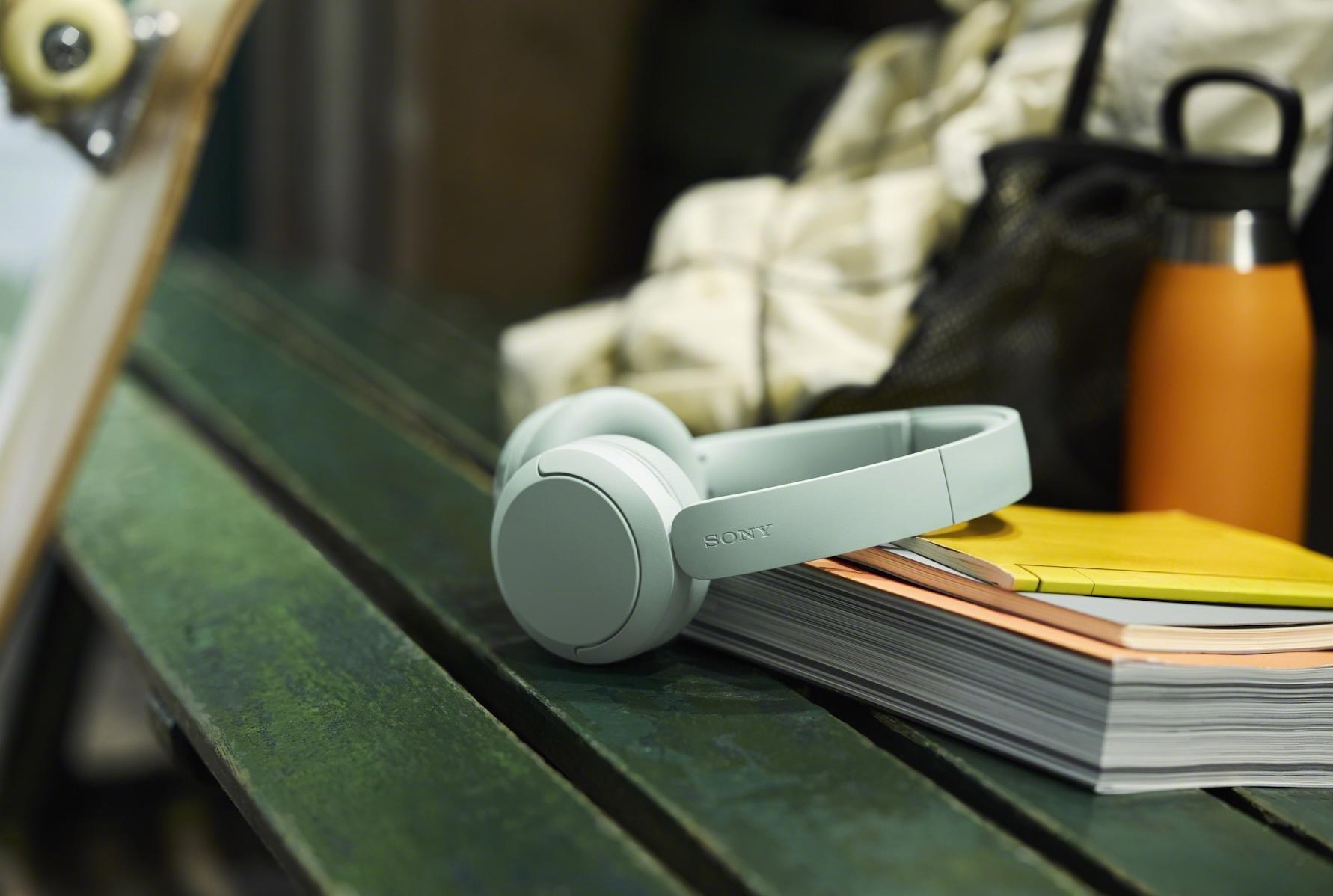 Green Sony WH-CH530 headphones resting against some books on a bench.